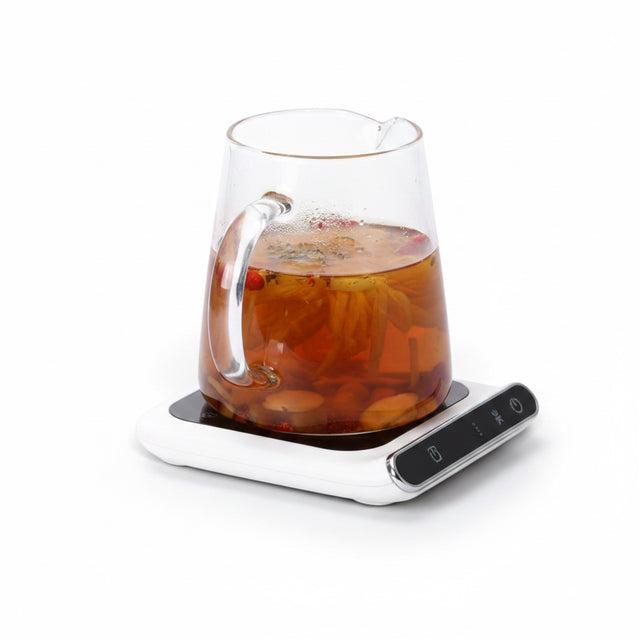 The Remote Desk white USB-powered mug warming plate with a glass carafe of herbal tea on a white background