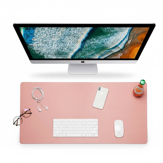 The Remote Desk waterproof pink leather-style desk mat with computer, keyboard, mouse, and phone on a white surface.